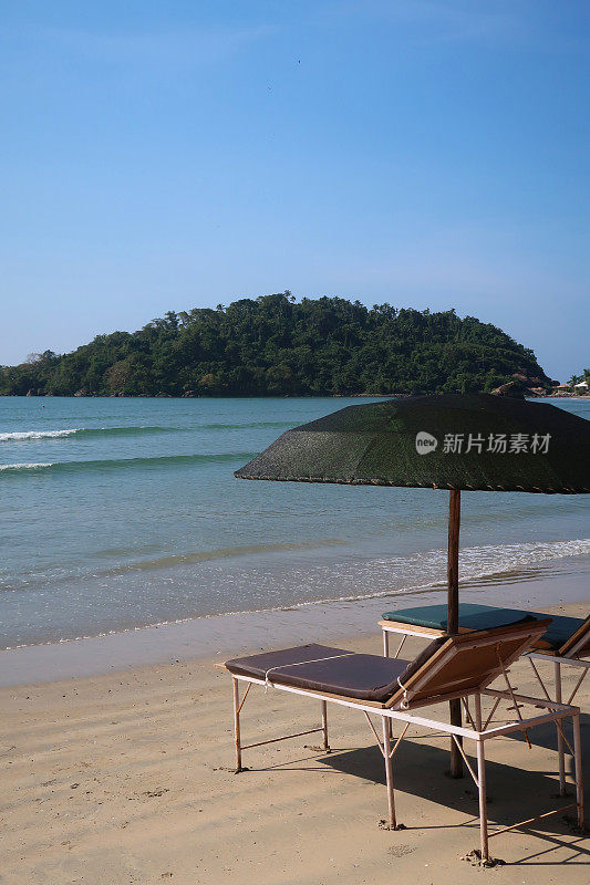 在热带沙滩上，木制太阳躺椅撑着阳伞，沙滩浴巾晒日光浴，在树荫下睡觉，木制太阳躺椅热带海滩假日海滨度假印度果阿/喀拉拉邦